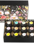 An open decorative box filled with individually wrapped grace & stella spa-quality bath bombs nestled in straw, featuring floral patterns on the interior lid.