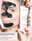 Woman applying a grace & stella blackhead removal peel-off mask to remove blackheads while holding the product tube.