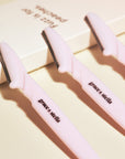 Three pink dermaplaning tools with black blades, labeled "flamingo" by grace & stella on a light background, ideal for facial exfoliation and removing peach fuzz.