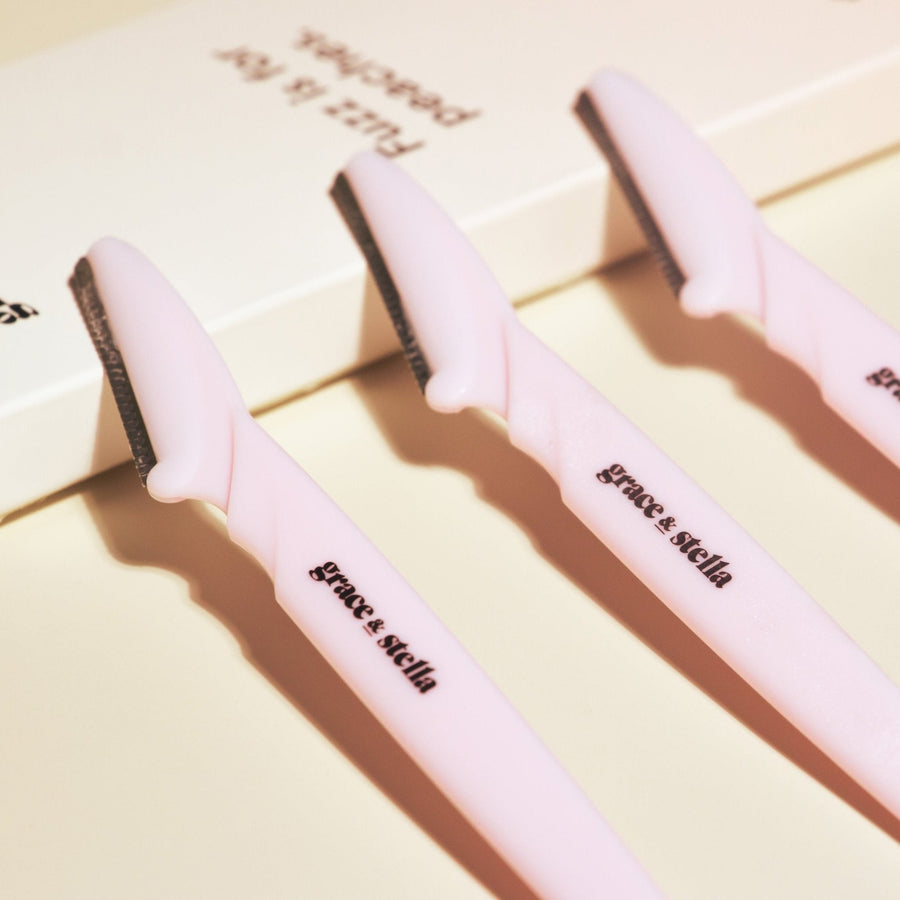 Three pink dermaplaning tools with black blades, labeled "flamingo" by grace & stella on a light background, ideal for facial exfoliation and removing peach fuzz.