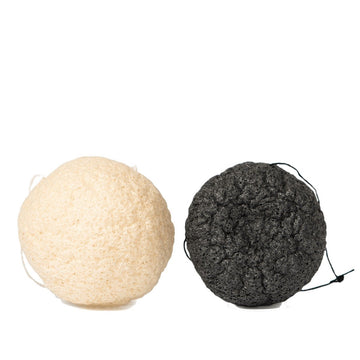 Two Grace & Stella Co. Konjac Facial Cleansing Sponges, one white and one black, isolated on a white background.
