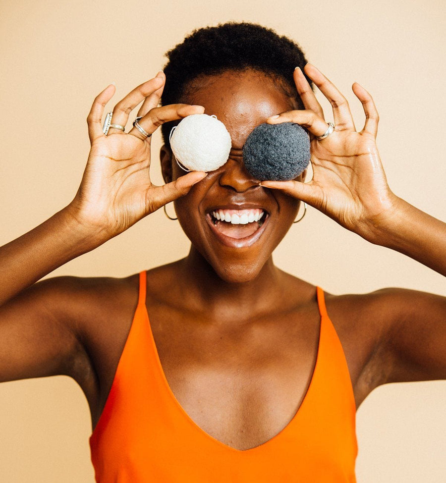 A person holding two Grace & Stella Co. Konjac Facial Cleansing Sponges over their eyes and smiling.