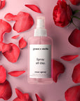 A bottle of la vie en rose set by grace & stella surrounded by fresh red tulips and petals on a pink background.