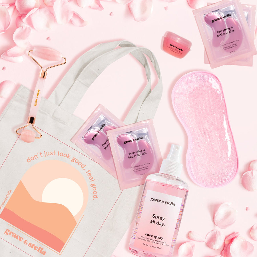 Flat lay of fresh Grace & Stella La Vie En Rose Set skincare products and spa accessories on a pink backdrop with rose petals.