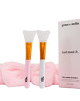 Two grace & stella co. silicone face mask brushes with pink handles alongside a matching pink headband, and a product box with the text "grace & stella - just mask it.
