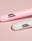 Two grace & stella co. branded silicone face mask brushes + headband with pink and white packaging on a pink background.