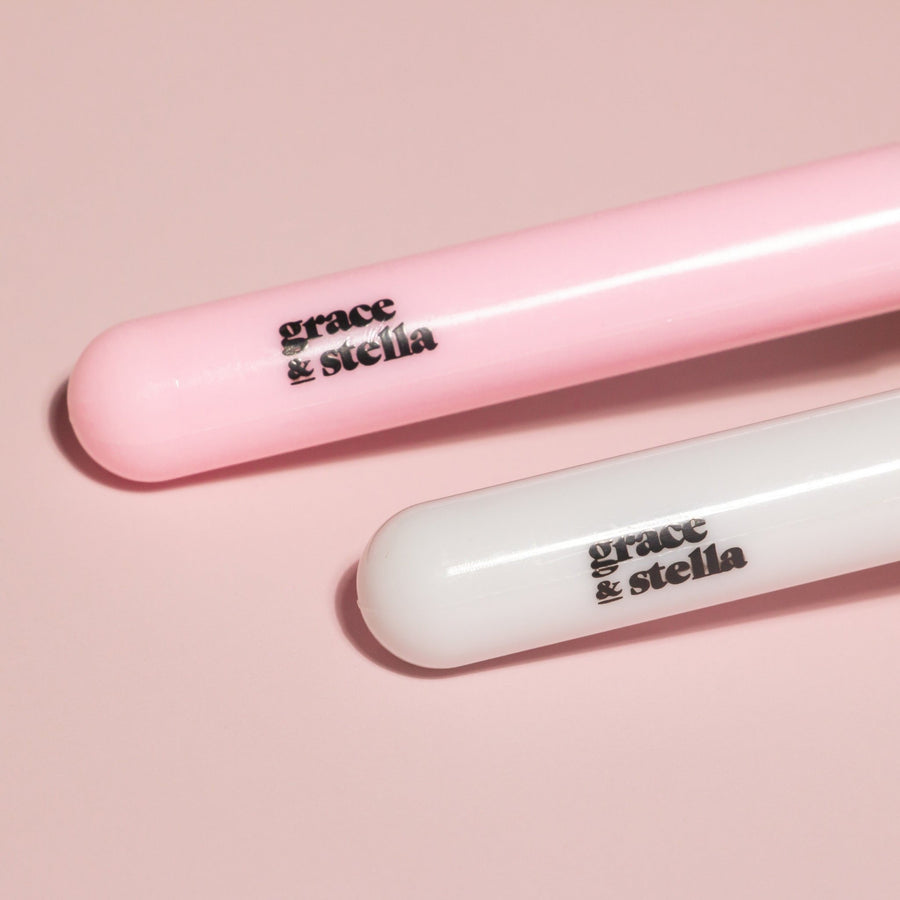 Two grace & stella co. branded silicone face mask brushes + headband with pink and white packaging on a pink background.