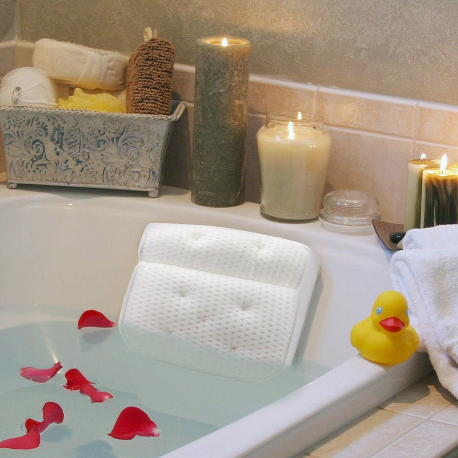 A relaxing and comfortable bathtub setup with a grace & stella bath pillow, rose petals, lit candles, and a rubber duck.