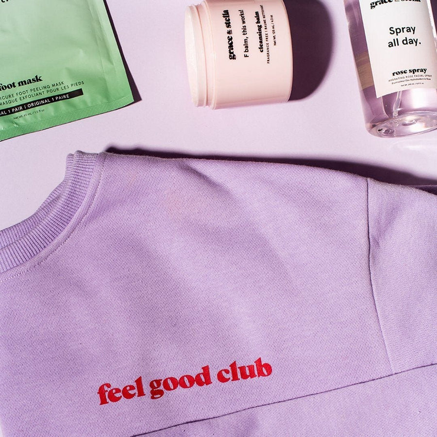 Lilac crewneck sweater from grace & stella's "Feel Good Club" line, accompanied by skincare products on a pink surface.