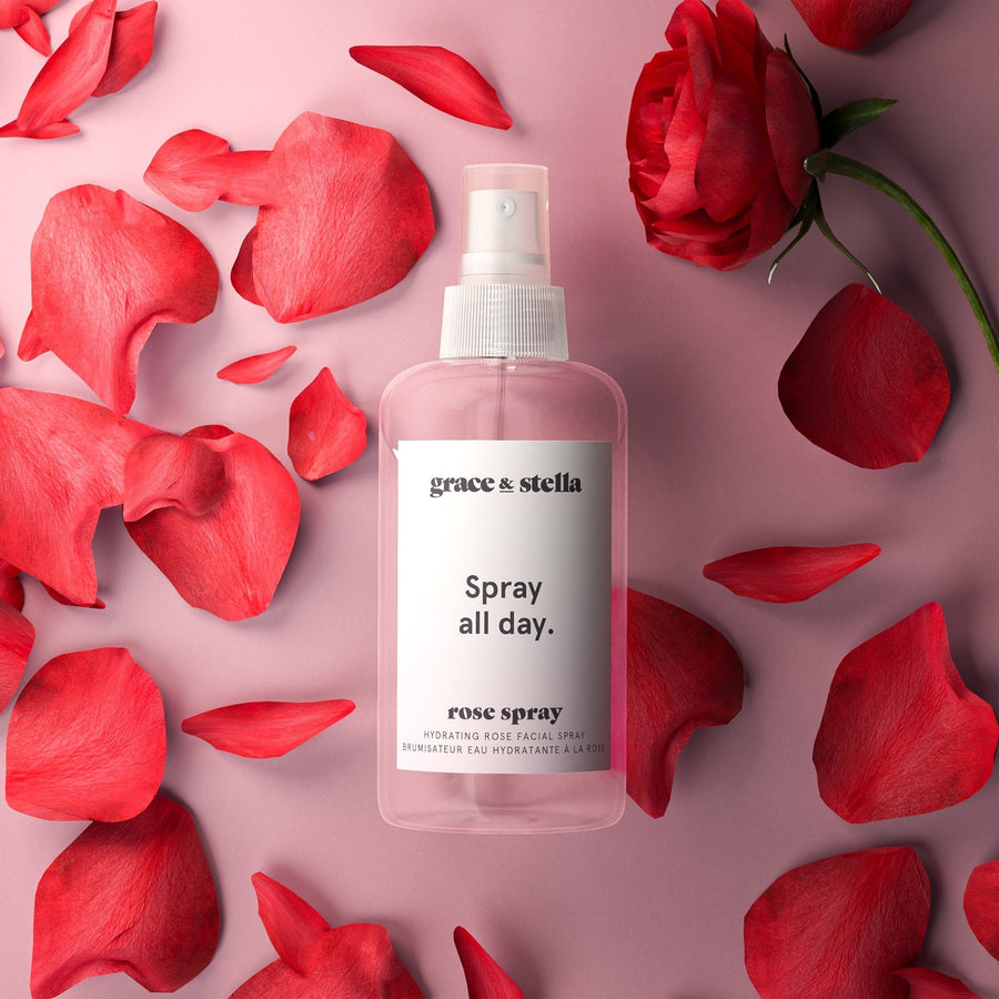 Bottle of grace & stella Anti-Inflammatory Rose Spray surrounded by red tulips and petals on a pink surface.