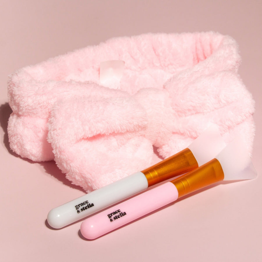 A pink fluffy headband with a grace & stella co. silicone face mask brush on top, perfect for applying face masks.